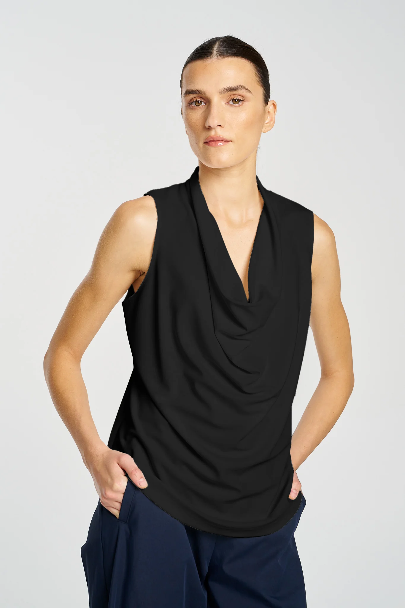 Woman wearing a black sleeveless top with a draped design on a light gray background