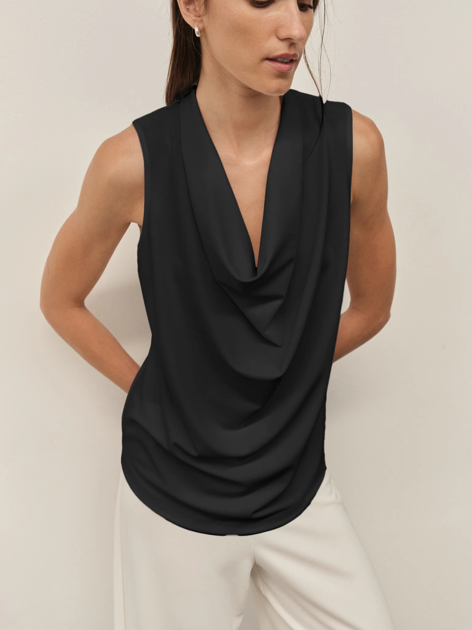 Woman wearing a black sleeveless top with a draped design against a plain background