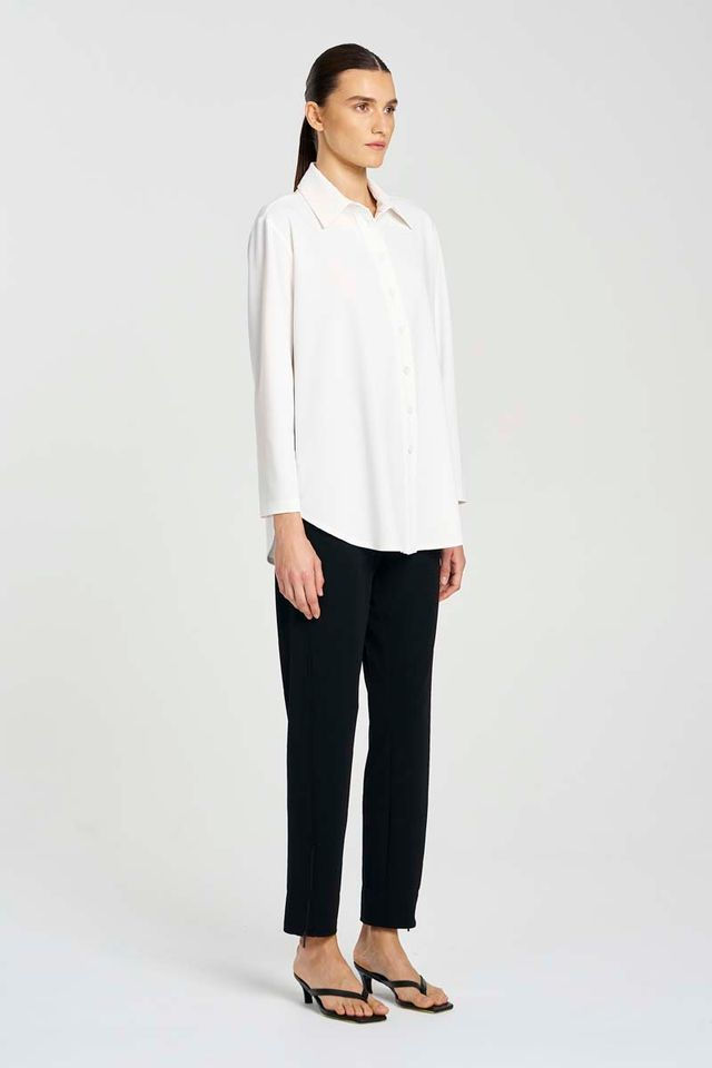 Woman wearing a white blouse and black pants on a plain background