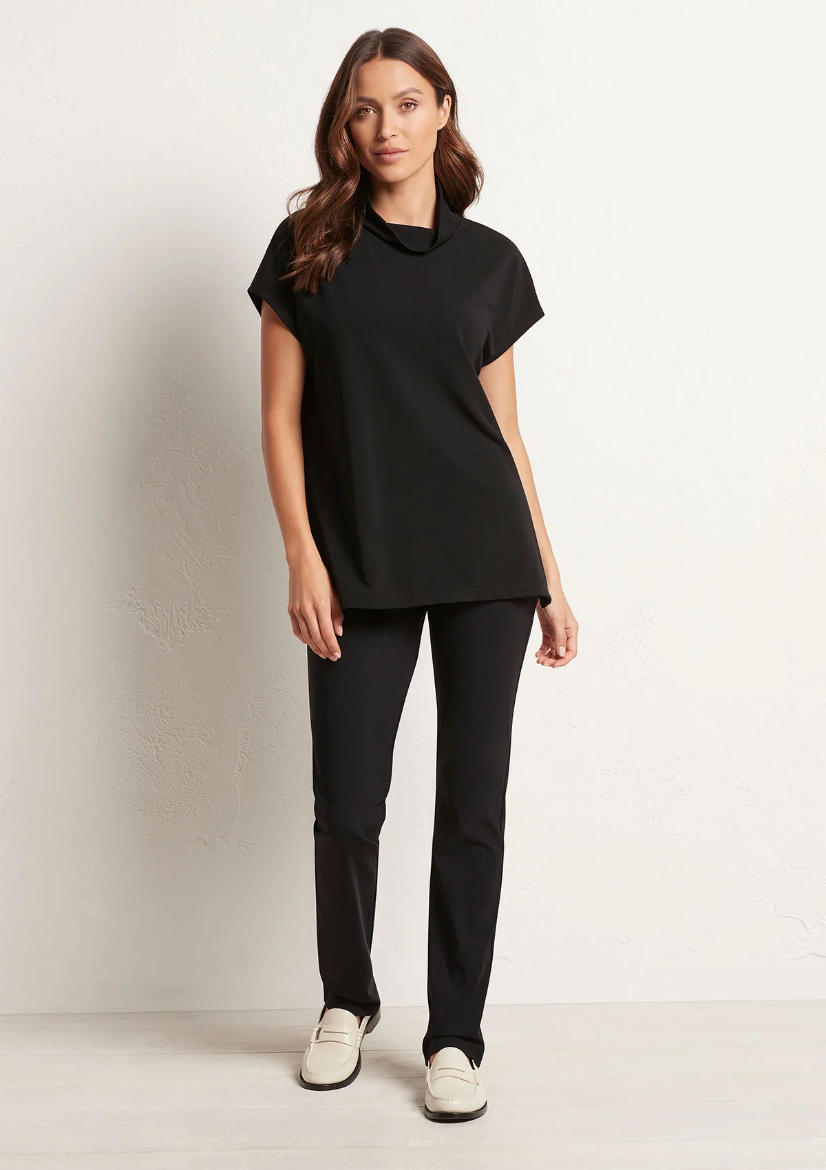 Woman wearing a black outfit with white shoes on a plain background