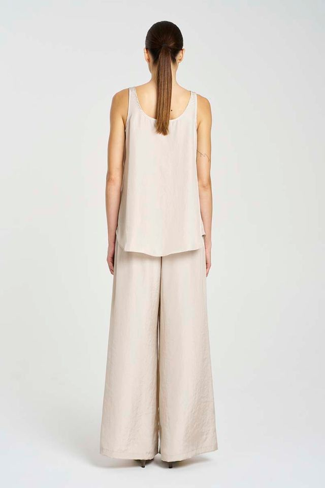 Woman wearing a beige sleeveless top and wide-leg pants on a white background