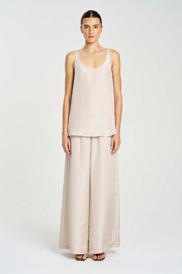 Woman wearing a beige sleeveless top and wide-leg pants on a white background