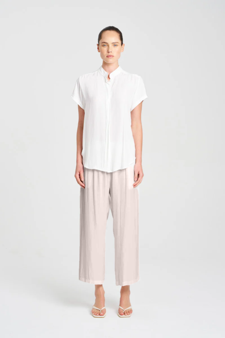 Person wearing a white shirt and light-colored pants on a plain background