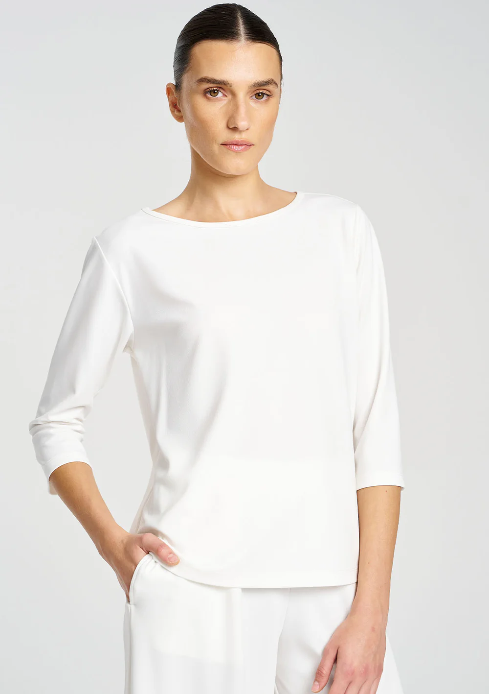 Woman wearing a white top and pants on a light gray background