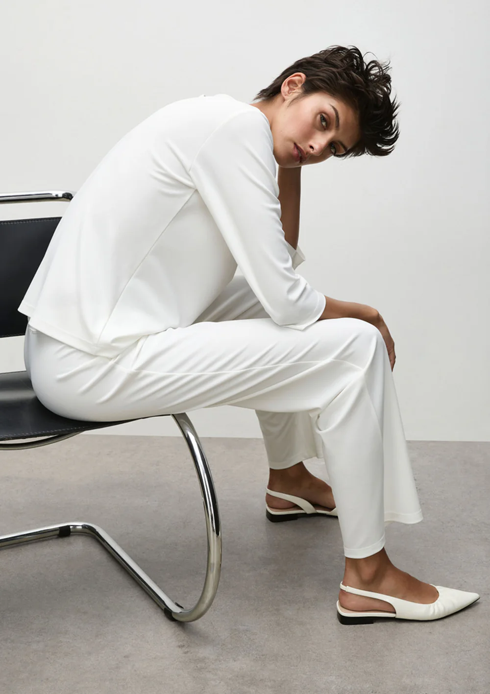 Person wearing a white outfit sitting on a chair in a minimalistic setting