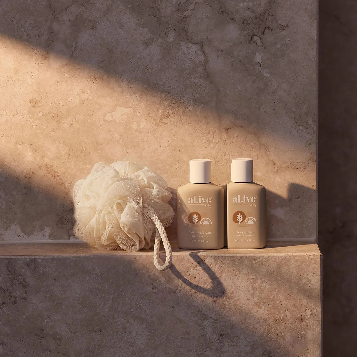 al.ive body Calming Oatmeal baby travel bottles and loofah on a stone ledge