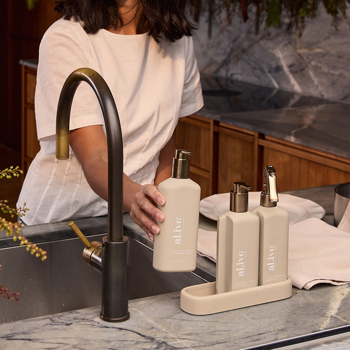 al.ive body Kitchen Trio Bronze Edition styled beside a kitchen sink with a dark bronze tap