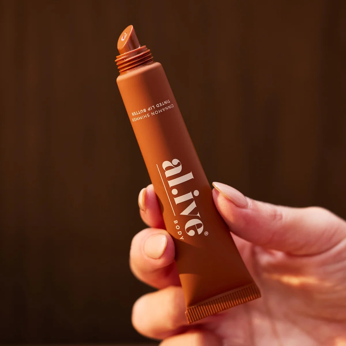 Hand holding al.ive body Cinnamon Shimmer Tinted Lip Butter