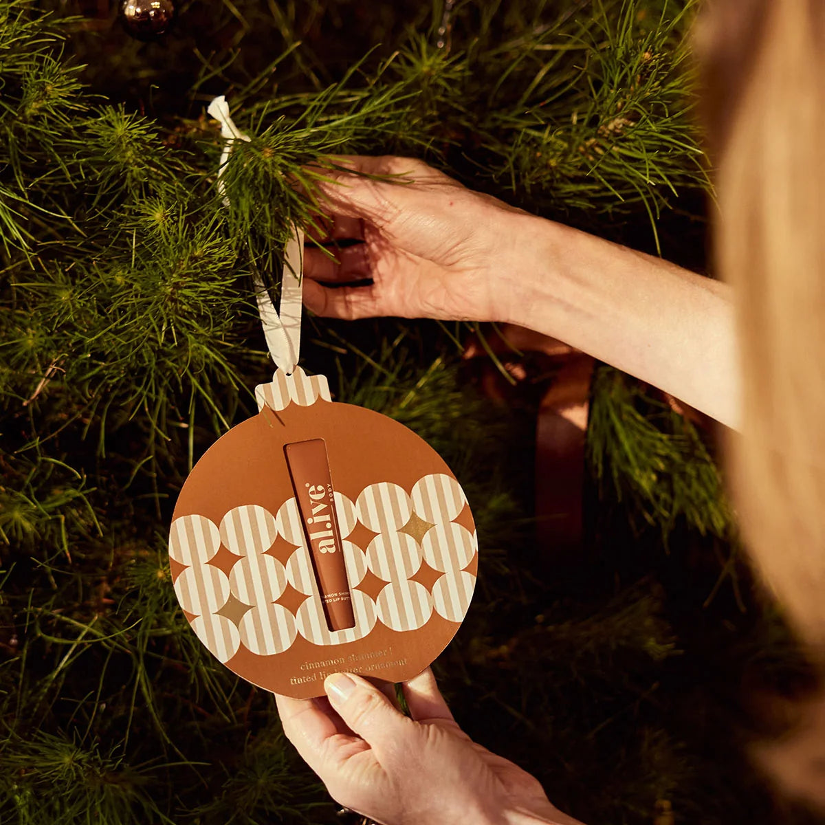 al.ive body Tinted Lip Butter Ornament hanging on a Christmas tree