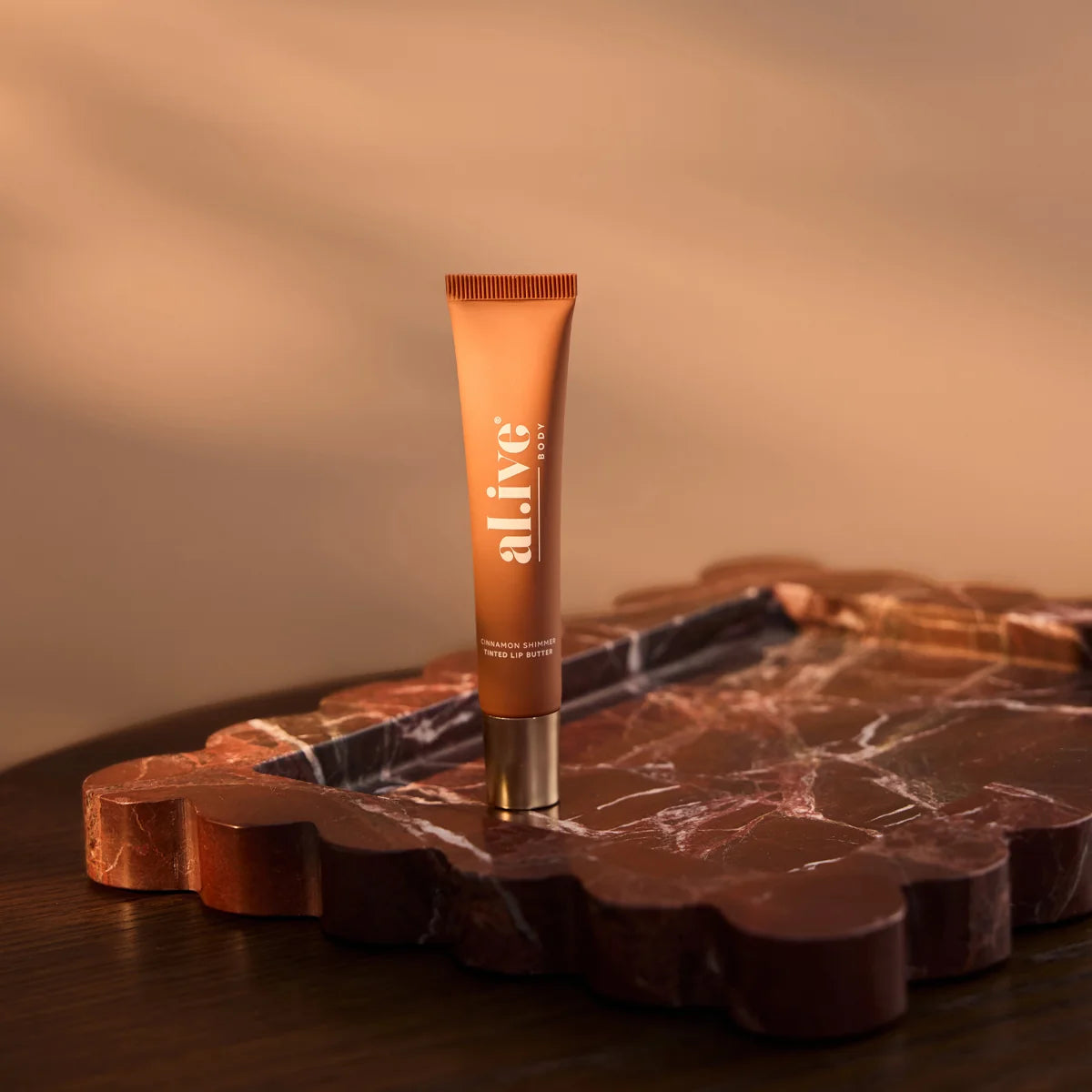 al.ive body Cinnamon Shimmer Tinted Lip Butter on a marble tray in warm light